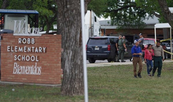 Three people walk away from a building with a police presense