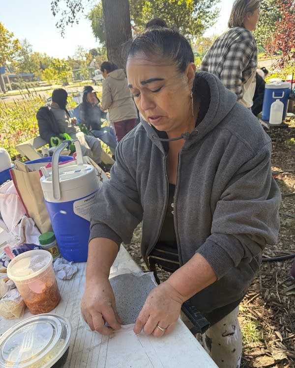 A woman shapes a tortilla on a picnic table on a fall day.