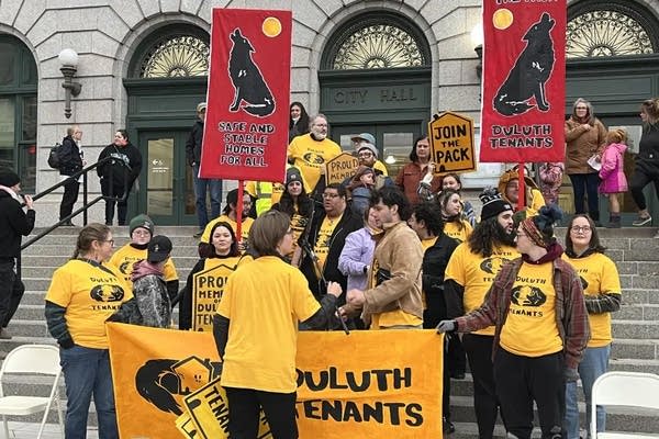 People from the group Duluth Tenants wear yellow shirts and hold up large signs.