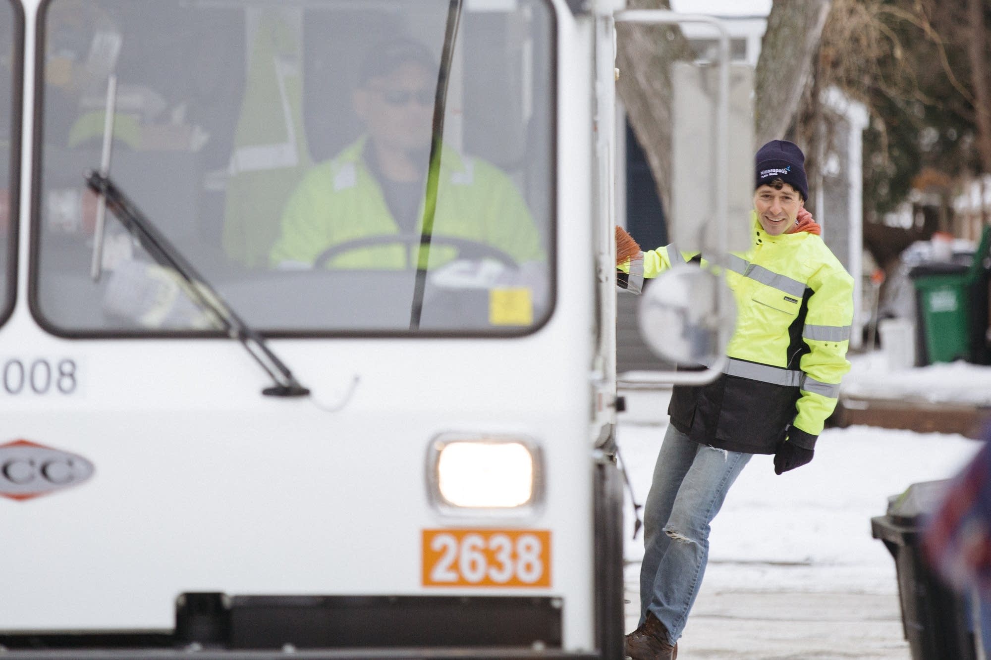 Jacob Frey rides on the back of an organics recycling truck.