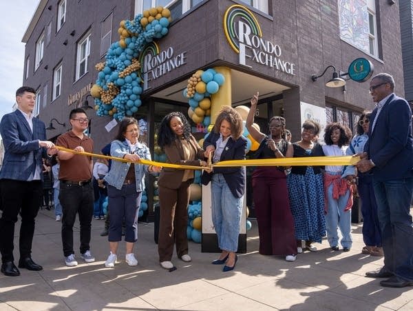 A group cuts a ribbon in front of a building with balloons. 