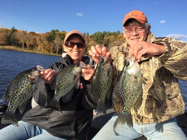 Two people hold up fish they caught at a lake. 