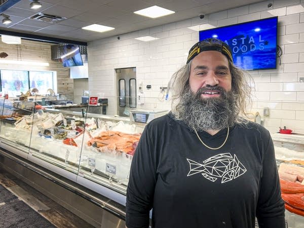 A man stands in a store, a counter full of seafood and ice behind him.