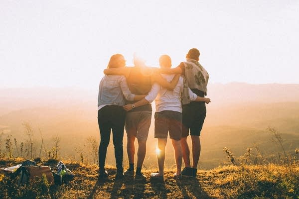 four people embrace while looking at sunset