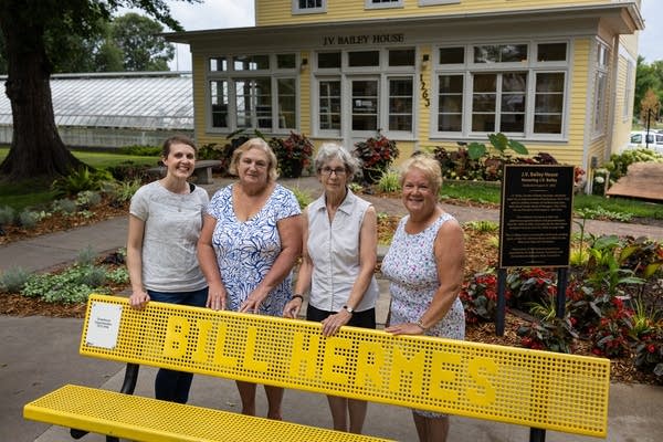 Four women pose next to a yellow bench
