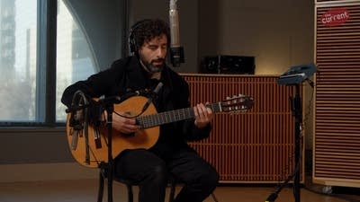 A musician sings and plays guitar in a recording studio