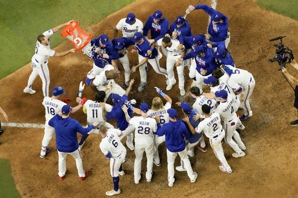 Players in white jerseys and blue jackets at home plate