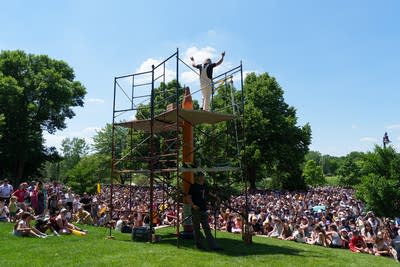 A man stands on top of a scaffolding with a giant pencle nearby.