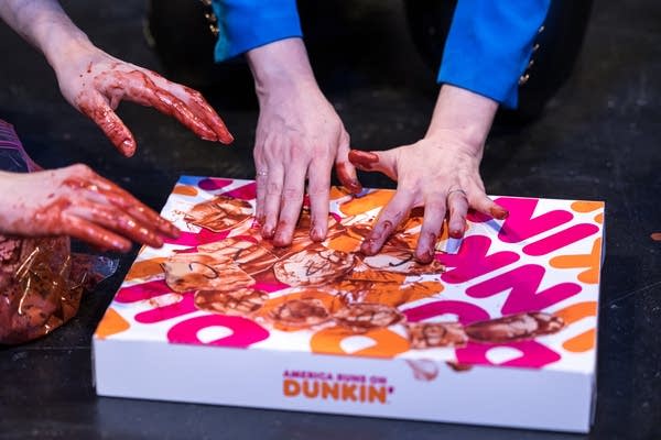 Hands covered in fake blood touch a donut box