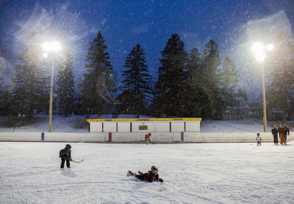 Snow falls and kids slide across the ice.