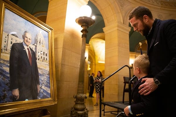 A man holds his son by the shoulders and looks at a painting. 