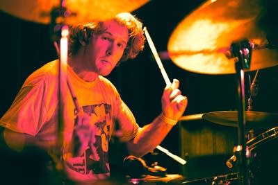 A man plays drums onstage in a music venue