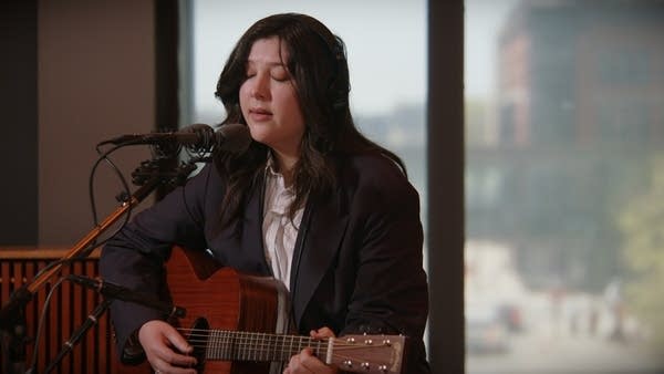 A woman sings and plays guitar in a recording studio