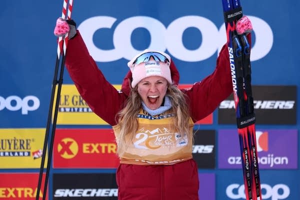 Jessie Diggens holds her skis and poles up in celebration.