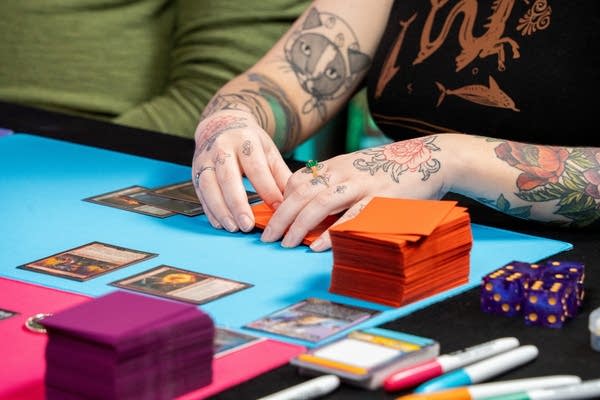 Two hands place playing cards on a blue playmat on a table.