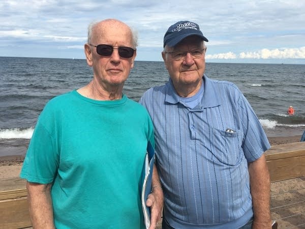 Two men stand on a beach. 