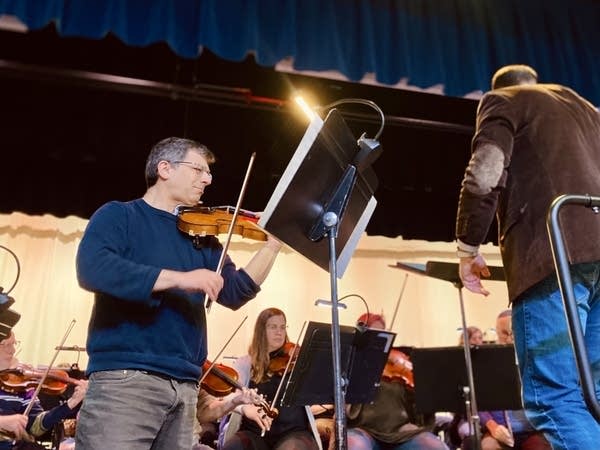 A musician stands in front of a symphony.