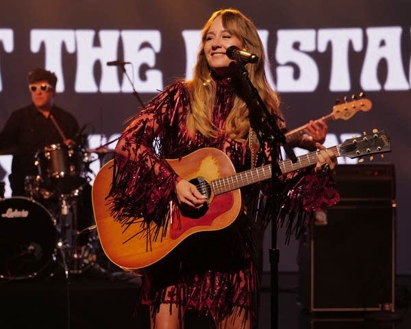 A woman sings and plays guitar on a television soundstage