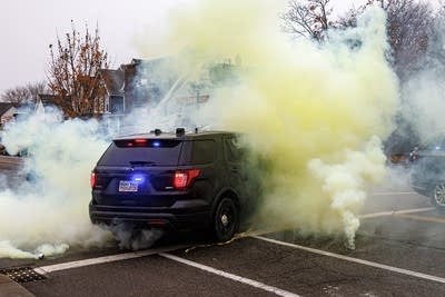 A police vehicle drives through a cloud of chemicals.