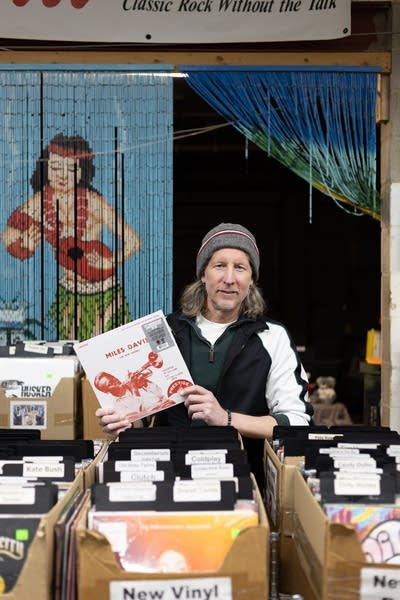 A man in a knitted cap holds up a Miles Davis album in a record store