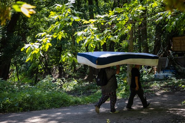 Two people walk with a mattress on their heads