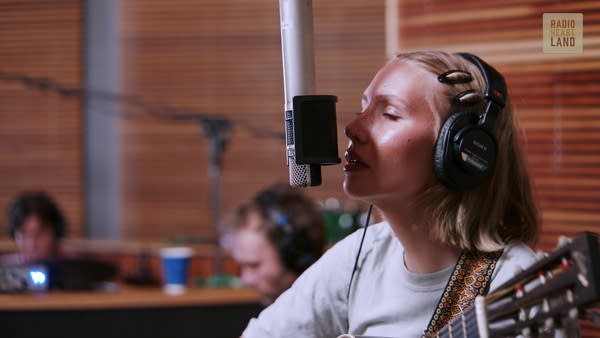 A musician sings and plays guitar in a recording studio