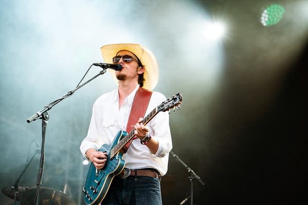 A musician sings and plays guitar on an outdoor stage
