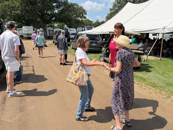 Three women talk with each other on a dirt path at a fair.