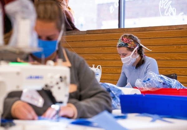 Two women wearing face masks sewing masks