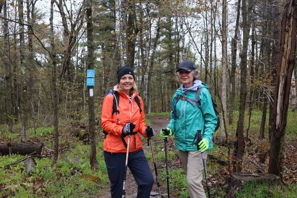A hiker in an orange jacket and a hiker in a teal jacket pose for a photo in the woods.