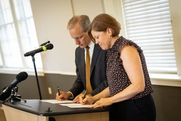 Two people sign pieces of paper