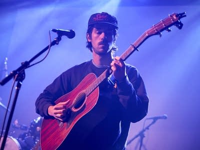 A man plays an acoustic guitar and sings into a microphone.