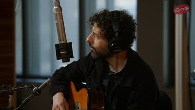 A musician sings and plays guitar in a recording studio