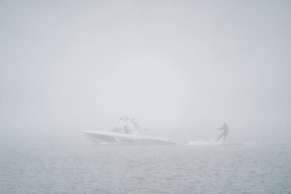 A person surfs behind a boat in the snow.