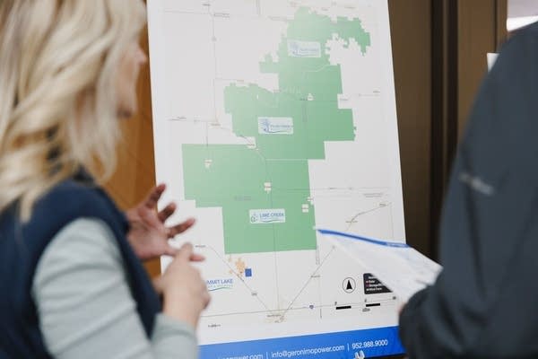 Two people talk in front of a map printed on a poster board.
