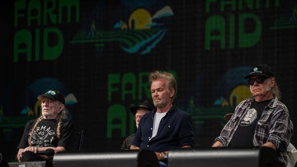 Willie Nelson, John Mellencamp, and Neil Young sit at a table during a press conference.
