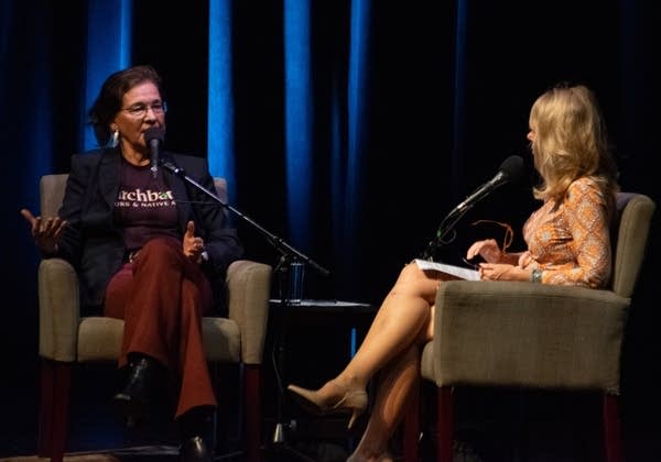 Two women sit on a stage with microphones.