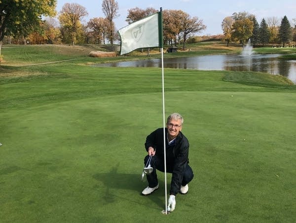 A man kneels down next to the cup on a golf green.