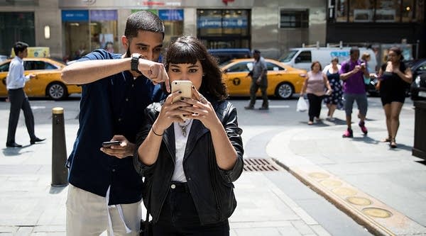  (L to R) Sameer Uddin and Michelle Macias use their smartphones outside of the Nintendo store in New York City. 