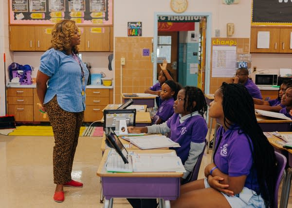 A woman in a denim shirt and leopard-print pants teaches a room of students.
