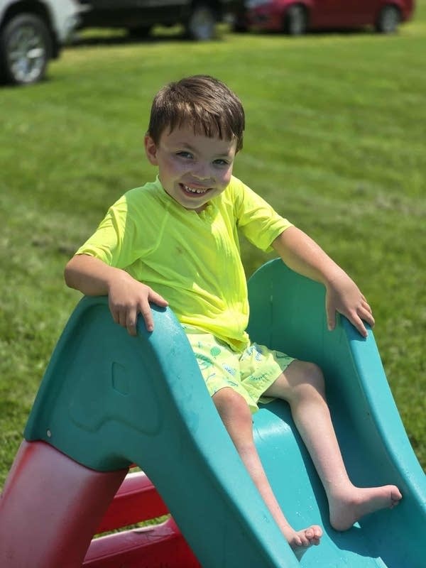 A young boy smiles for a photo while sitting on a plastic slide.