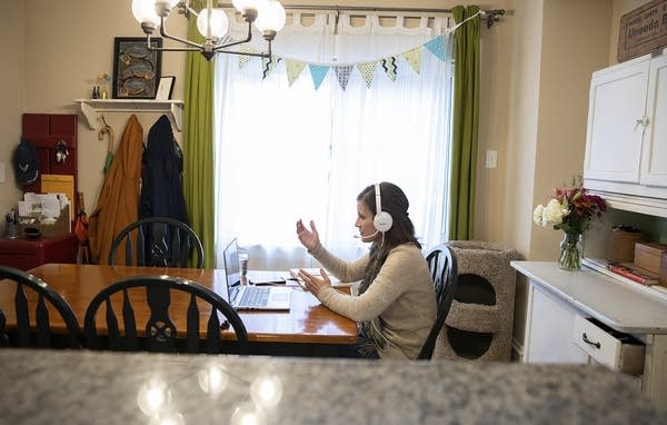 A woman gestures as she sits in front of a laptop at a kitchen table.