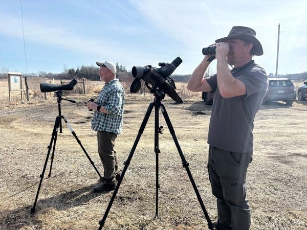 Two people look through spotting scopes and binoculars.