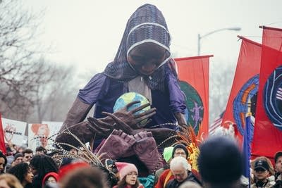 A giant woman holding earth is carried.