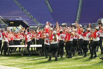 A marching band performs on the field of a football stadium.