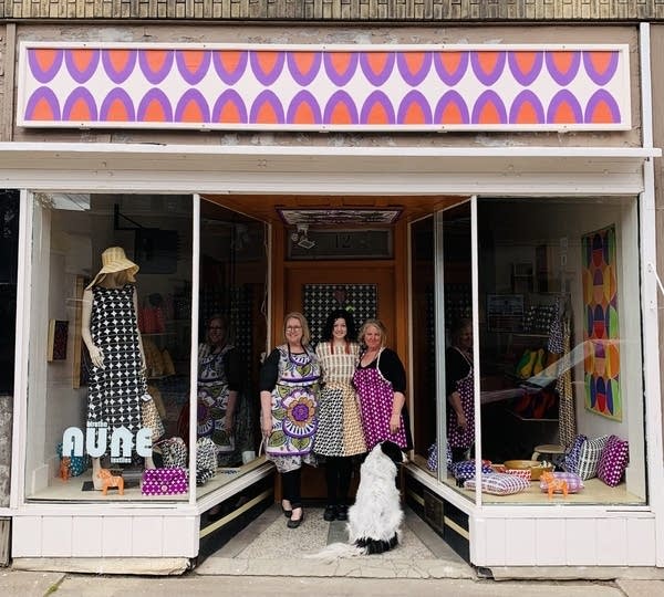 Three people stand with a dog in front of storefront