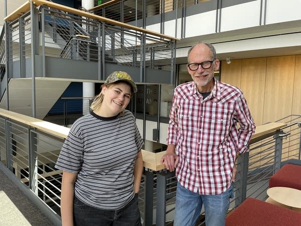 Two people stand in an atrium for a photo together
