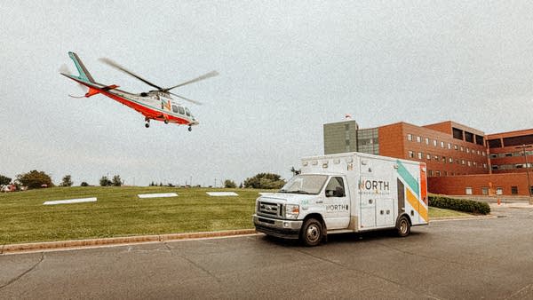 A helicopter in the air and an ambulance parked nearby for North Memorial Health.