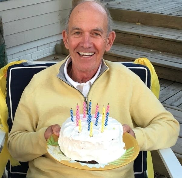 A man sitting in a chair holds a birthday cake, smiling.