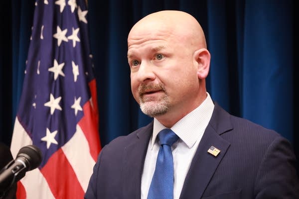 man in blue tie speaks near flag